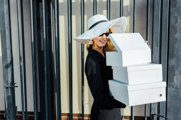 Happy young woman in stylish clothes holding stack of white shoe boxes — Stock Photo