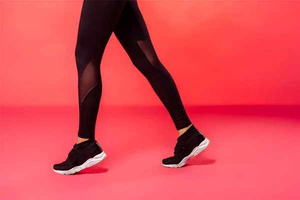 Abgeschnittenes Bild einer Sportlerin, die in schwarzen Leggings auf Rot läuft — Stockfoto