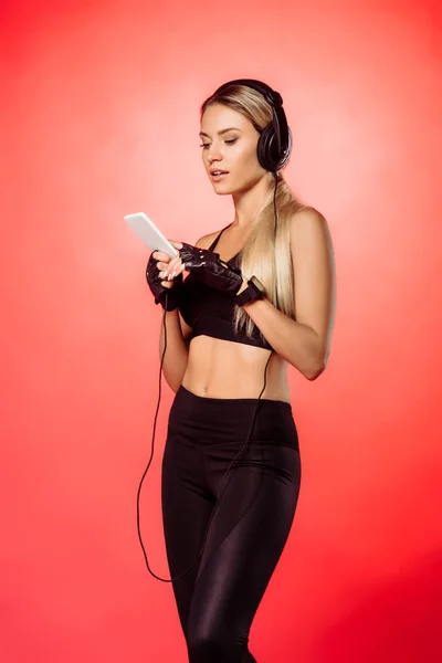 Deportista atractiva escuchar música con teléfono inteligente aislado en rojo - foto de stock
