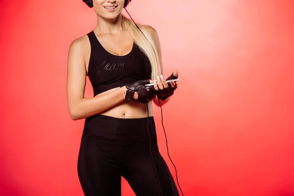 Cropped image of sportswoman listening music with smartphone isolated on red — Stock Photo