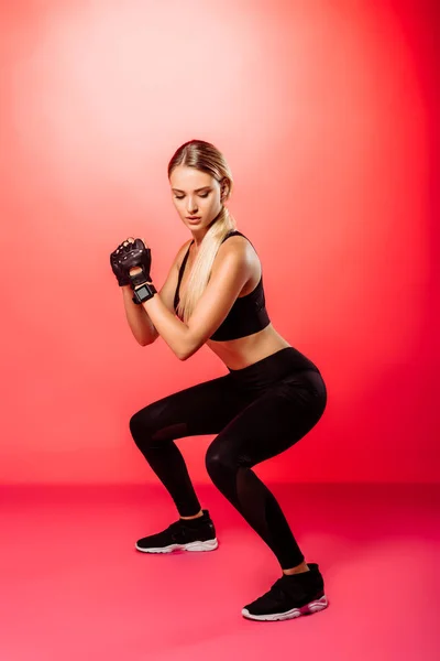 Attraente sportivo formazione e fare squat su rosso — Foto stock