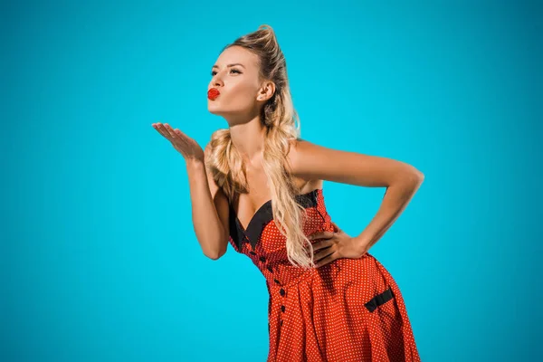 Attractive young pin up woman in retro style clothing blowing kiss isolated on blue — Stock Photo