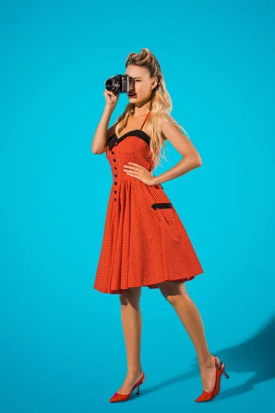Красива жінка в сукні в стилі пін-ап з фотоапаратом на синьому фоні — стокове фото
