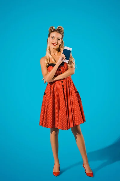 Mujer sonriente en pin up ropa de estilo con billete y pasaporte sobre fondo azul - foto de stock