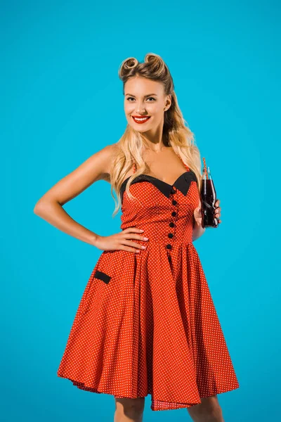 Retrato de sorrindo pin up mulher em vestido vintage com bebida de refrigerante em garrafa de vidro no fundo azul — Fotografia de Stock