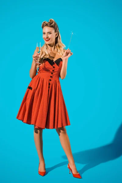 Jolie femme en pin up vêtements avec scintillant et verre de champagne sur fond bleu — Photo de stock