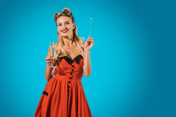 Pretty pin up woman in vintage clothing with sparkler and glass of champagne on blue backdrop — Stock Photo