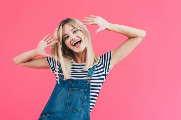 Lächelndes schönes Mädchen in Jeans, das die Zunge herausstreckt, gestikuliert und in die Kamera schaut, isoliert auf rosa — Stockfoto