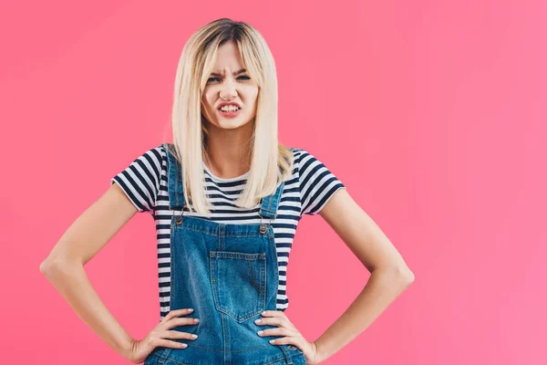 Irritated girl in denim overall looking at camera isolated on pink — Stock Photo