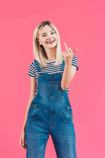 Smiling beautiful girl in denim overall showing middle finger isolated on pink — Stock Photo