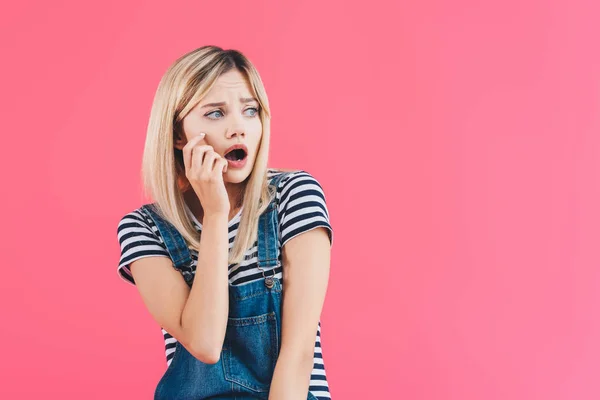 Schockiertes Mädchen in Jeans berührt Wange und blickt isoliert auf rosa — Stockfoto
