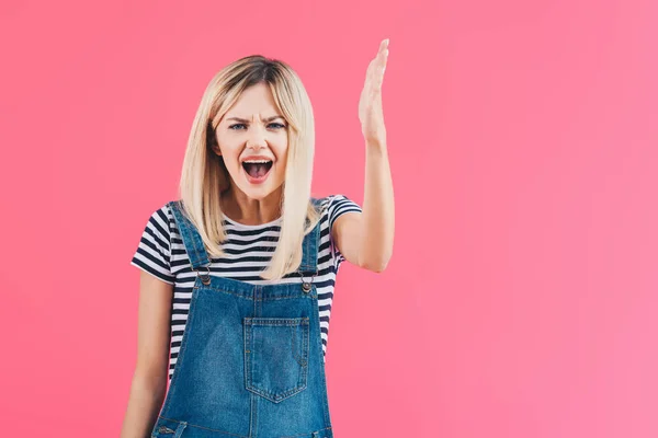 Angry girl in denim overall yelling and gesturing isolated on pink — Stock Photo