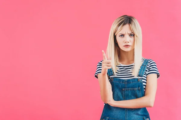 Irritated girl in denim overall pointing on something isolated on pink — Stock Photo
