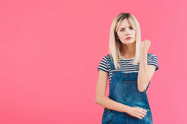 Сердитая девушка в джинсах с фистом на розовом фоне — стоковое фото