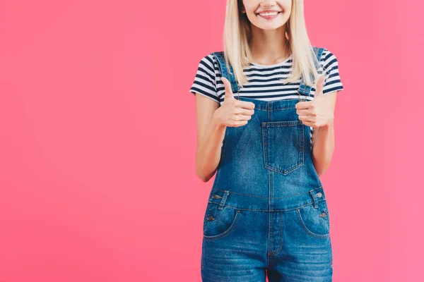 Cropped image of smiling girl in denim overall showing thumbs up isolated on pink — Stock Photo