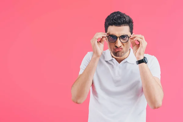 Gutaussehender Mann grimmig, Brille angefasst und Kamera isoliert auf rosa — Stockfoto