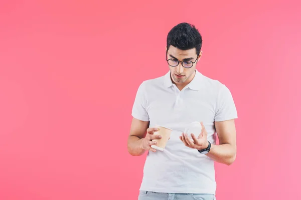 Schöner Mann schaut in Einweg-Kaffeetasse isoliert auf rosa — Stockfoto