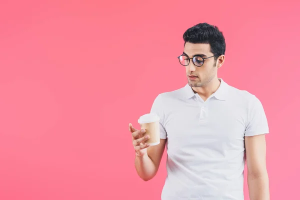 Schöner Mann schaut auf Einweg-Kaffeetasse in der Hand isoliert auf rosa — Stockfoto