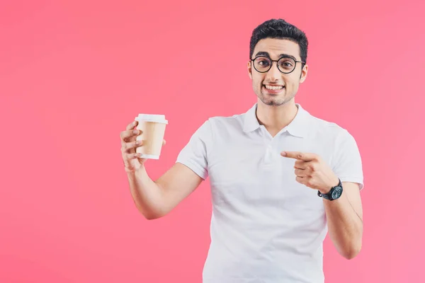 Hombre guapo feliz señalando en taza de café desechable aislado en rosa - foto de stock