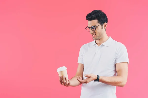 Bel homme grimaçant regardant le café dans une tasse en papier isolé sur rose — Photo de stock