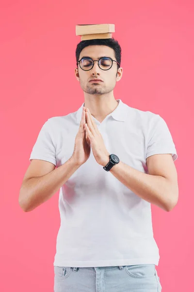 Étudiant beau avec les yeux fermés et geste namaste méditant avec des livres sur la tête isolé sur rose — Photo de stock