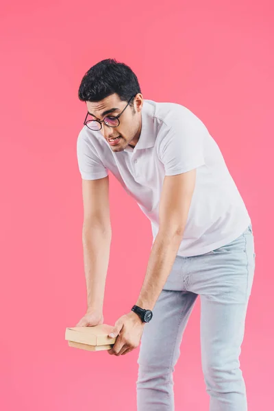 Handsome grimacing student holding heavy books isolated on pink — Stock Photo