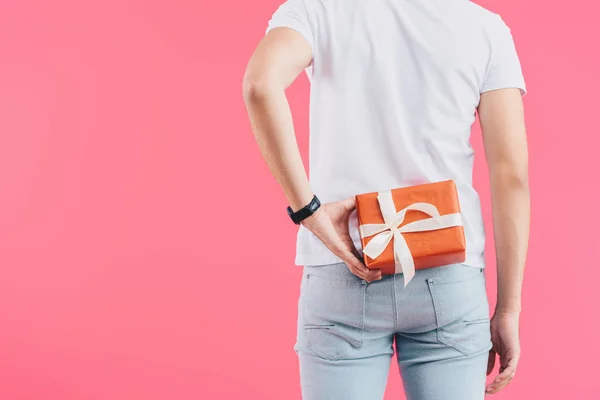 Imagen recortada del hombre sosteniendo caja de regalo detrás de la espalda aislado en rosa - foto de stock