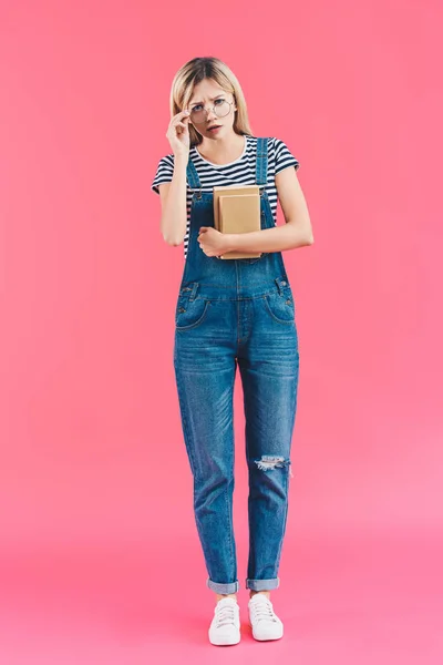 Молодой студент в очках с книгами, смотрящий на камеру на розовом фоне — стоковое фото