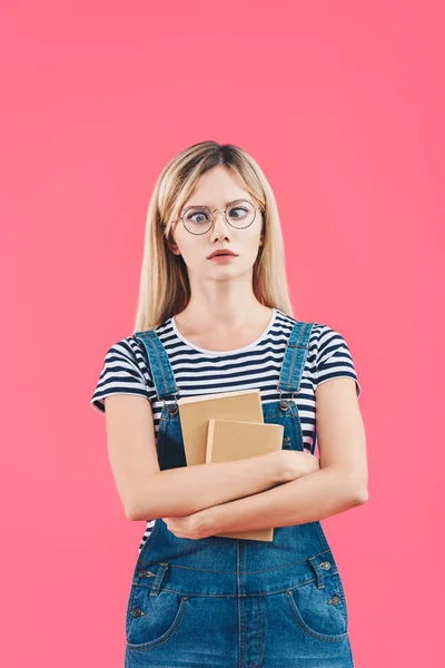 Портрет гримасы молодой студент в очках с книгами изолированы на розовый — стоковое фото