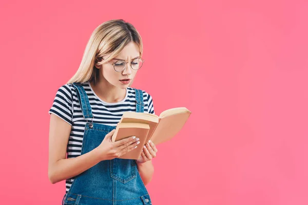 Портрет сфокусированного ученика в очках с книгами, изолированными на розовом — стоковое фото