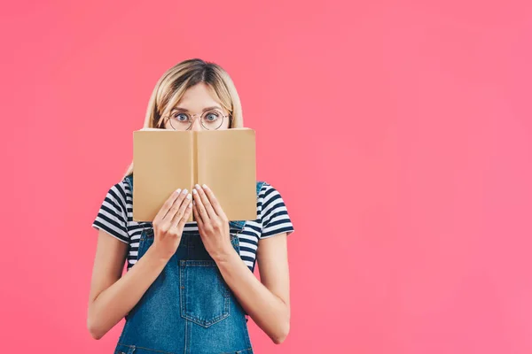 Vista oscurecida de la mujer en gafas con libro aislado en rosa - foto de stock