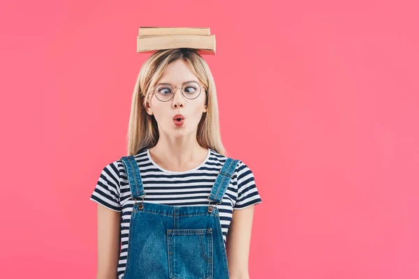 Portrait of young grimace student in eyeglasses with books on head isolated on pink — Stock Photo