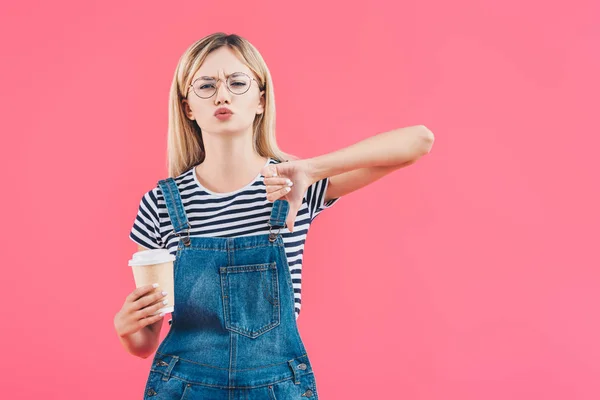 Retrato de jovem mulher com café para ir mostrando polegar para baixo isolado em rosa — Fotografia de Stock