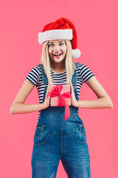 Portrait de femme souriante en santa claus chapeau tenant cadeau isolé sur rose — Photo de stock