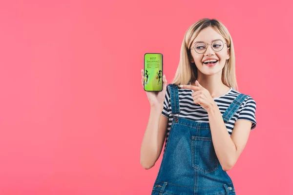 Porträt einer lächelnden Frau mit Brille, die auf das Smartphone zeigt, mit bestem Einkaufsschild auf rosa — Stockfoto