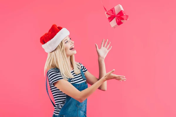 Junge Frau mit Weihnachtsmann-Hut wirft Geschenk auf rosa — Stockfoto