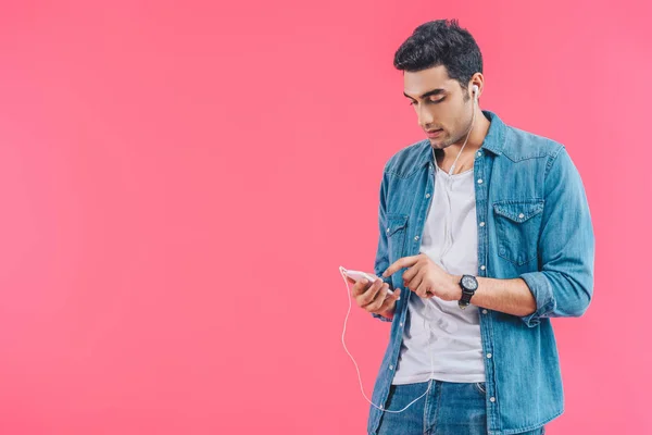 Портрет молодого чоловіка зі смартфоном, який слухає музику в навушниках ізольовано на рожевому — стокове фото