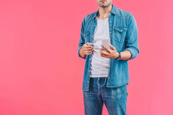 Cropped shot of man with smartphone listening music in earphones isolated on pink — Stock Photo