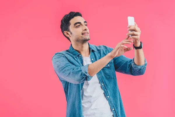 Retrato de un joven tomando selfie en un teléfono inteligente aislado en rosa - foto de stock
