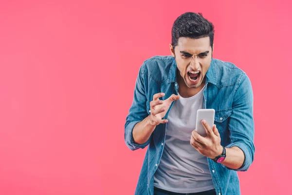 Retrato del hombre enojado mirando el teléfono inteligente en la mano aislado en rosa - foto de stock