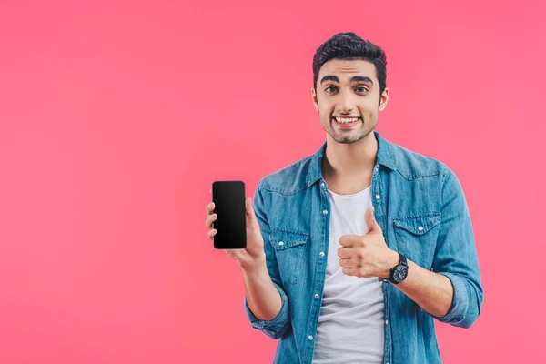 Jeune homme souriant faisant geste pouce vers le haut et montrant smartphone avec écran vide isolé sur rose — Photo de stock