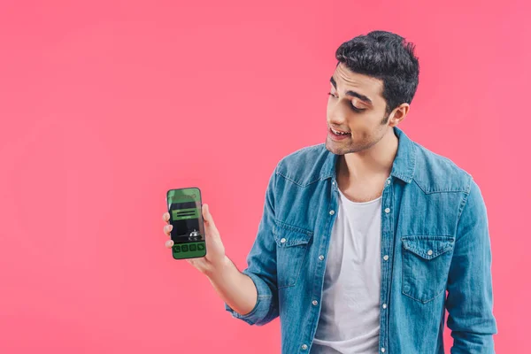 Lächelnder junger Mann zeigt Smartphone mit Buchung isoliert auf pink — Stockfoto