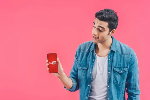 Smiling young man showing smartphone with youtube website isolated on pink — Stock Photo