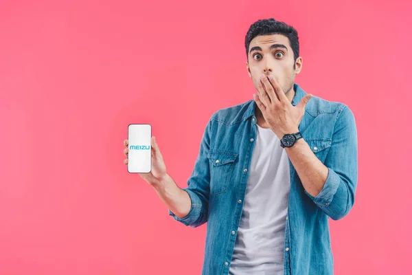 Chocado jovem cobrindo boca à mão e meizu smartphone isolado em rosa — Fotografia de Stock