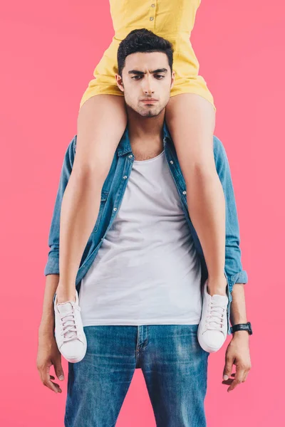 Cropped image of woman sitting on shoulders of upset boyfriend isolated on pink — Stock Photo