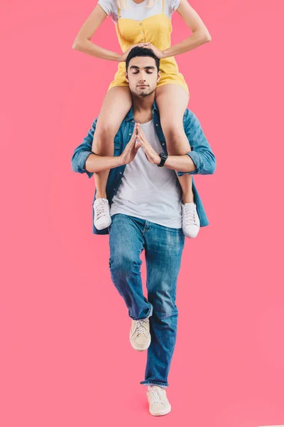 Cropped image of woman sitting on shoulders of boyfriend while he meditating with closed eyes isolated on pink — Stock Photo