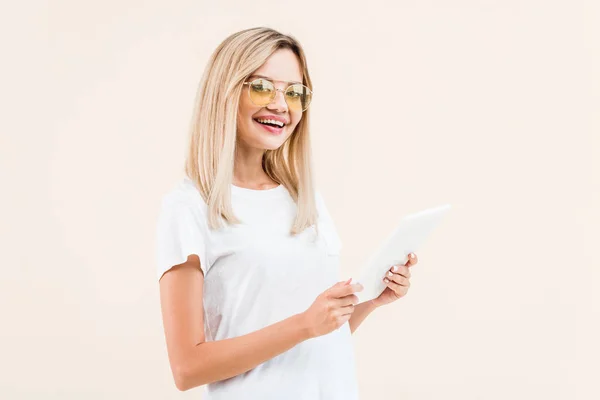 Mujer elegante sonriente en gafas usando tableta digital aislada en beige - foto de stock