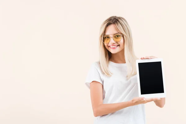 Glückliche junge Frau in Brille zeigt digitales Tablet mit leerem Bildschirm isoliert auf beige — Stockfoto