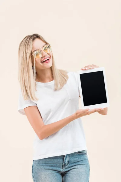 Fröhliche junge Frau in stylischer Brille zeigt digitales Tablet mit leerem Bildschirm isoliert auf beige — Stockfoto