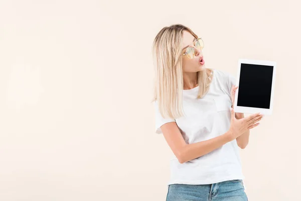 Surprised stylish woman in eyeglasses showing digital tablet with blank screen isolated on beige — Stock Photo